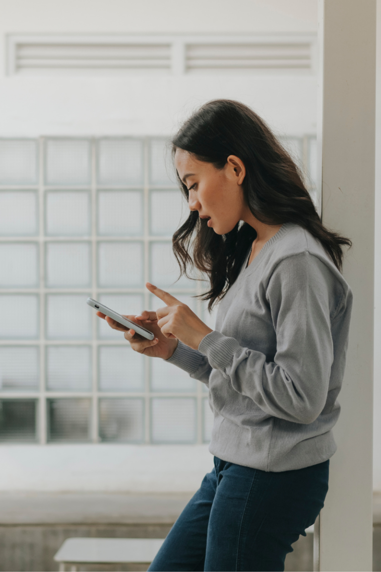 Woman casually scrolling on her phone while leaning against a wall, visually representing the message behind stop wasting time quotes and the struggle with everyday distractions.