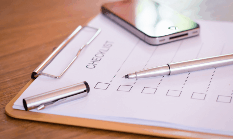 Flat lay of a printed client onboarding checklist with a pen and phone on a wooden desk—ready for next steps.