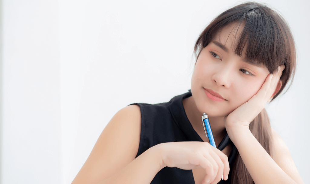 Woman resting her head on her hand with a pen, appearing thoughtful while journaling with prompts. Captures a moment of reflection and self-awareness using guided questions.