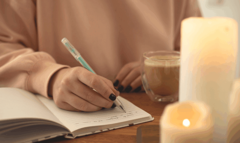 Cozy journaling setup with a notebook, coffee, and candles, illustrating an intentional ritual for journaling with prompts. Evokes warmth, focus, and grounded self-inquiry.