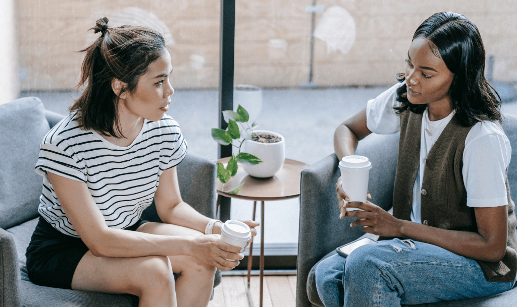 Two women sitting on cozy chairs, engaged in a deep conversation over coffee—capturing the essence of virtual coffee chats brought offline.